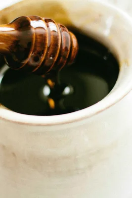 Ein Honiglöffel taucht in einen Topf mit dunklem Honig ein.