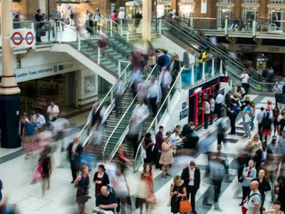 A busy London train station with blurred figures moving on stairs and escalators.