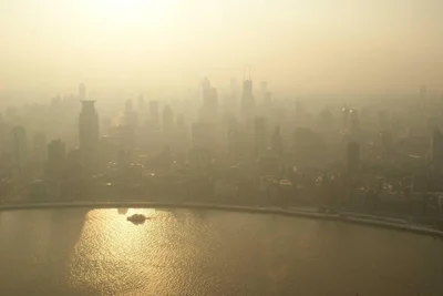 Eine Stadtlandschaft mit Wolkenkratzern ist in dichten Smog gehüllt, ein Fluss fließt im Vordergrund.