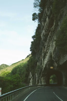 Eine Straße führt durch einen Tunnel, der in einen bewachsenen Felsen gehauen wurde.