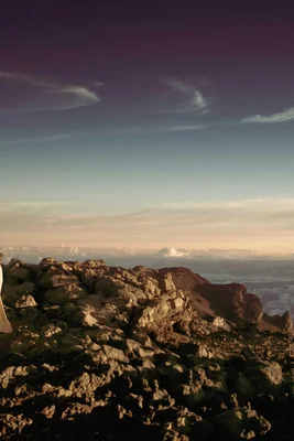 Felsiger Berggipfel mit Blick auf eine Wolkendecke unter einem gestreiften Himmel.